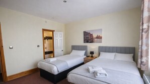 A hotel room with two single beds, a bathroom with a mirror and sink, and a painting of a cityscape on the wall. - Hotel 65 (London)