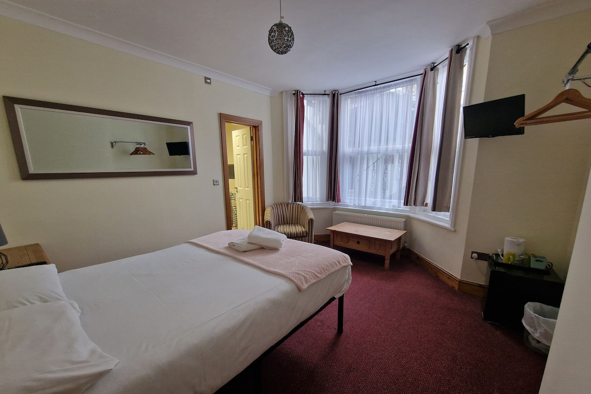 A hotel room with a bed, a chair, a small table, a mirror, and a window with curtains.