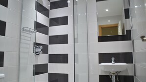 A bathroom with black and white tiles, a glass shower enclosure, and a sink with a mirror above it. - Hotel 65 (London)