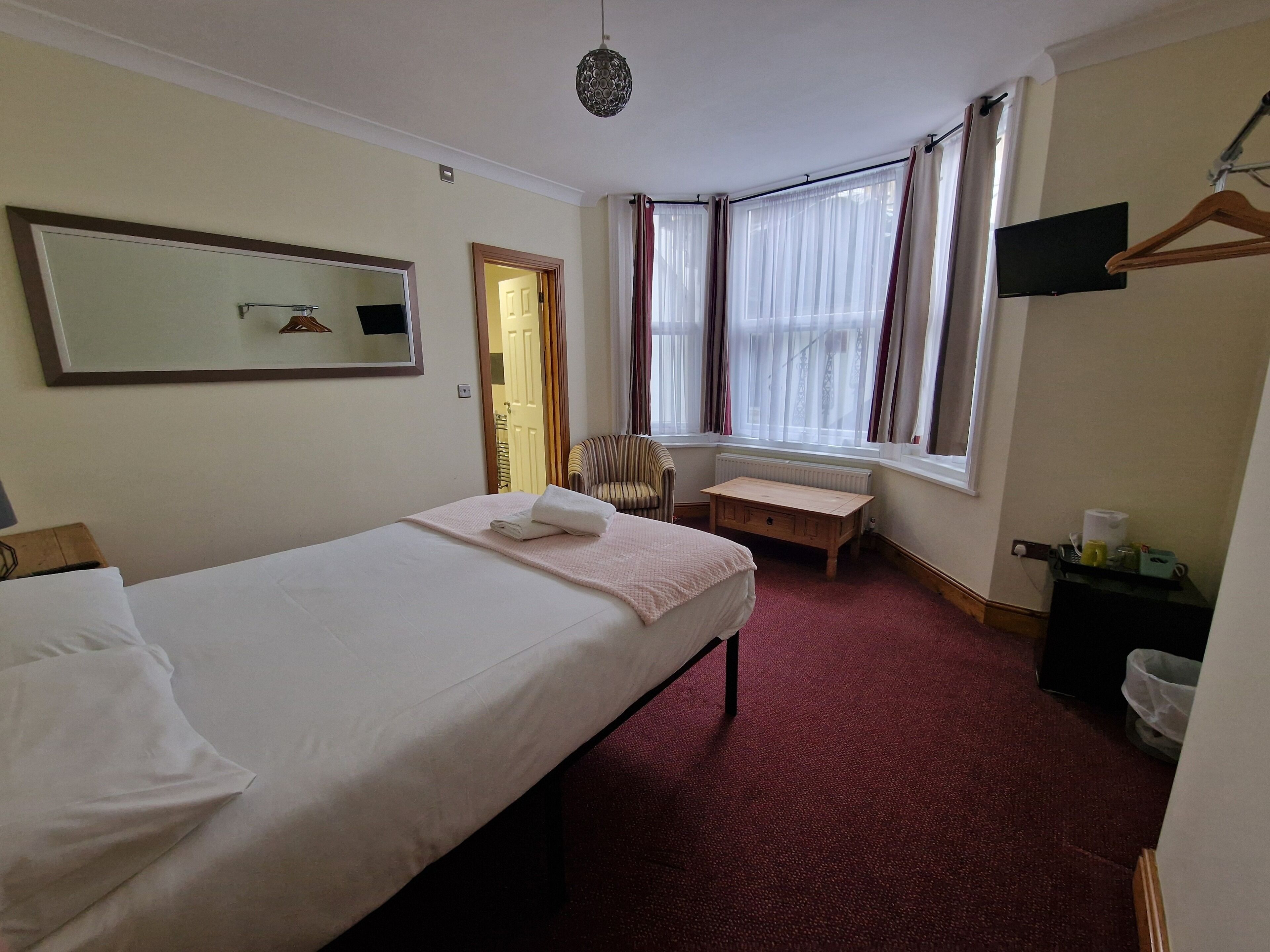Ein Hotelzimmer mit Bett, Stuhl, kleinem Tisch, Spiegel und einem Fenster mit Vorhängen.