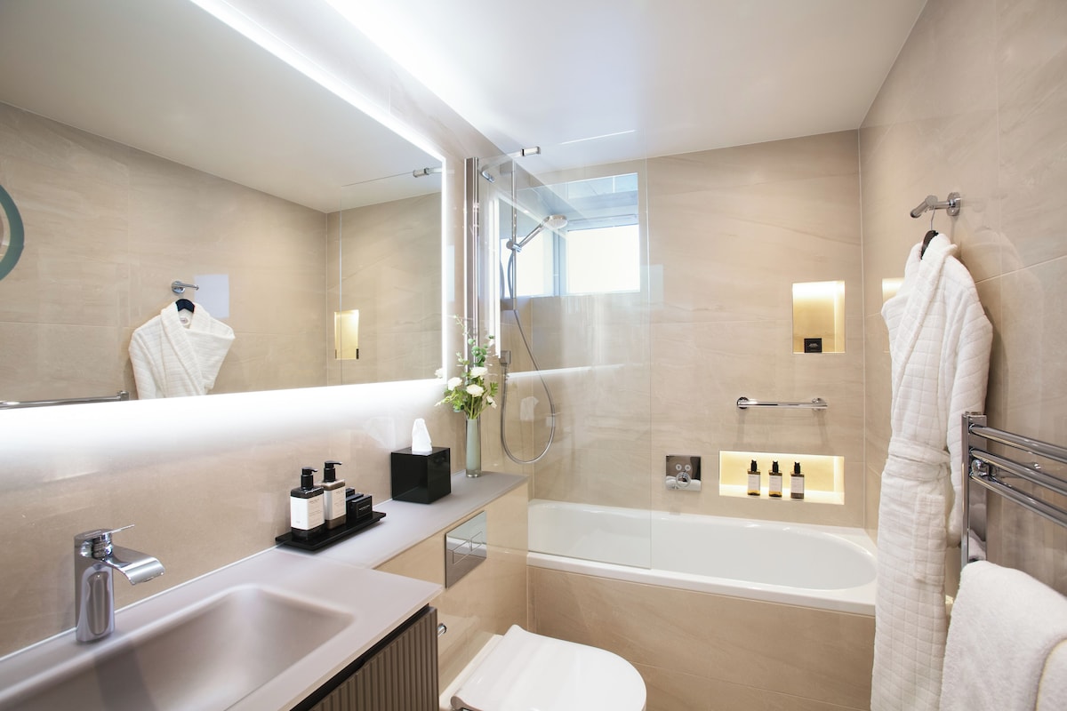 A modern bathroom with a glass-enclosed shower, a bathtub, a vanity with a sink and mirror, and a towel rack.