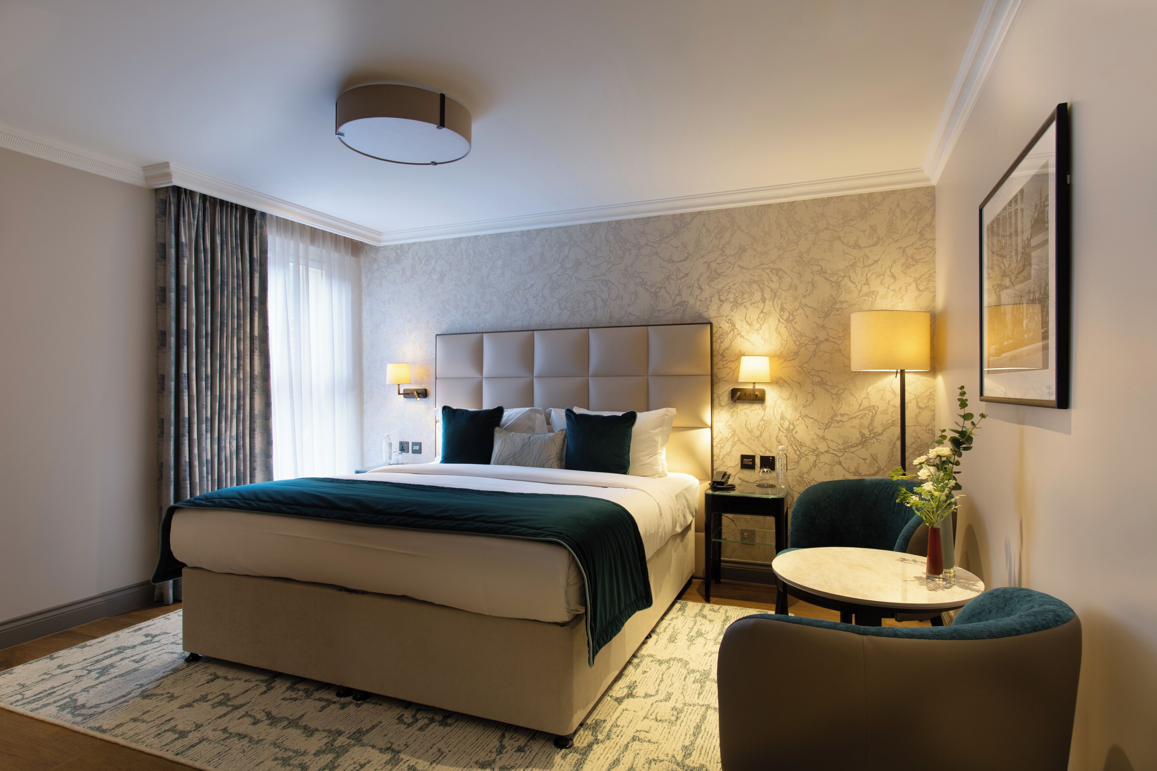 A hotel room with a large bed, bedside lamps, a small table, and a chair.