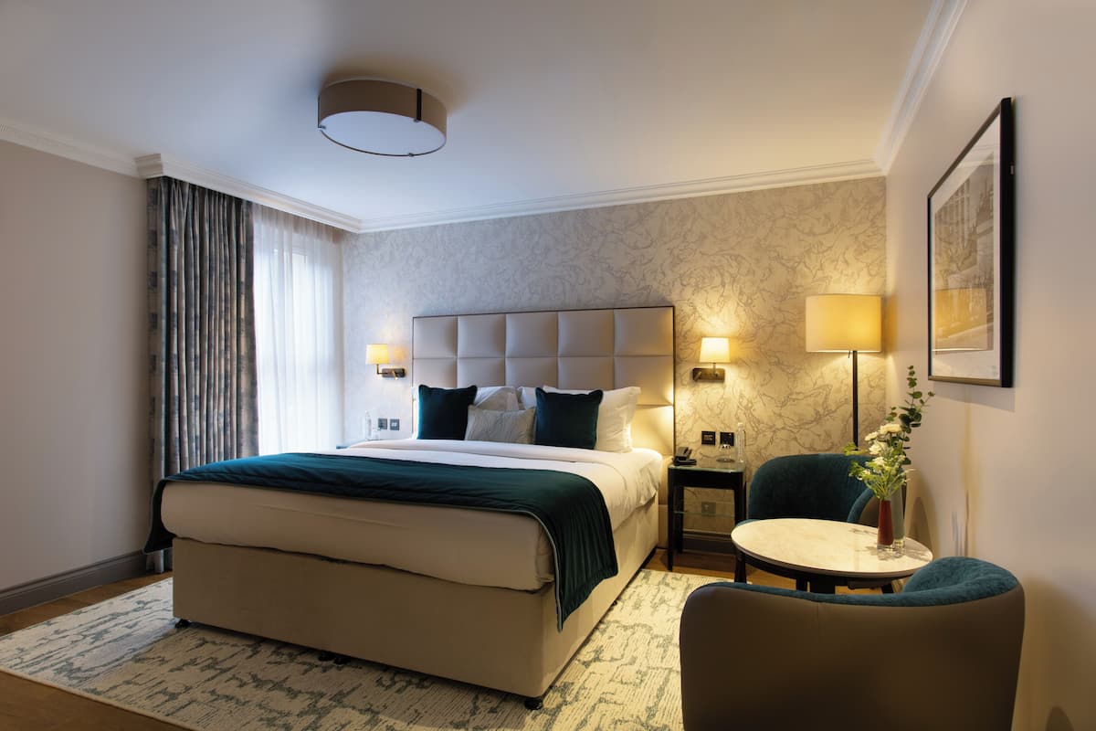 A hotel room with a large bed, bedside lamps, a small table, and a chair.