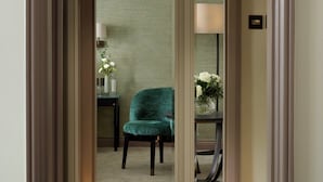 Une pièce avec un fauteuil vert, une petite table sur laquelle est posé un vase de fleurs et une lampe sur une table de chevet.