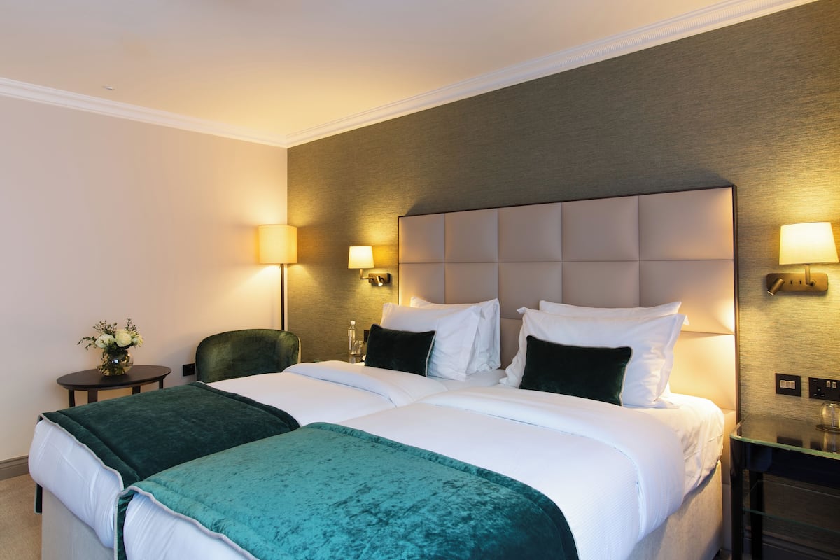 A hotel room with a large bed, two bedside tables, a green chair, and wall-mounted lamps.