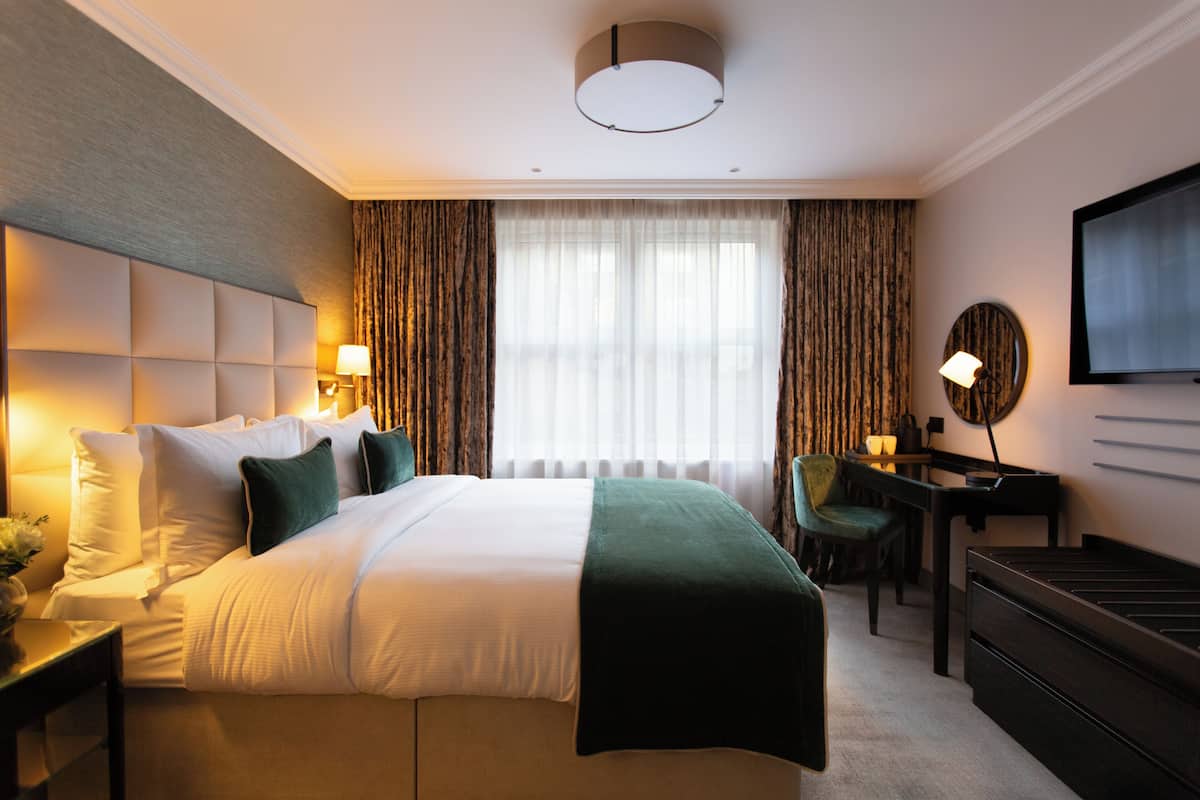 A hotel room with a large bed, a desk, a chair, a television, and a window with curtains.