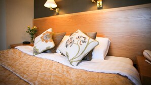 A neatly made bed with floral pillows, a wooden headboard, and two wall-mounted lamps. - The Tomich Hotel (Beauly)