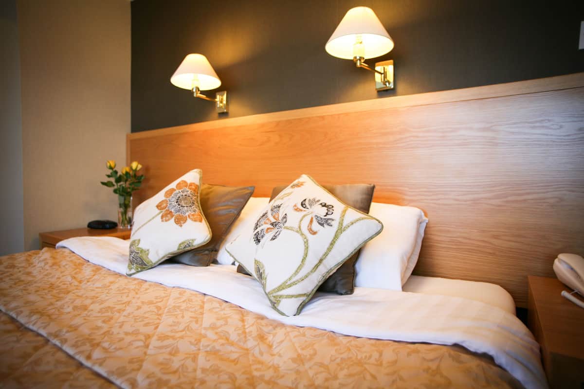 Ein ordentlich bezogenes Bett mit blumigen Kissen, einem hölzernen Kopfteil und zwei Wandleuchten.