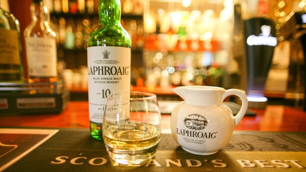A bottle of Laphroaig whisky, a glass, and a jug on a table with the text "Scotland's Best". - The Tomich Hotel (Beauly)