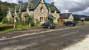 A stone building with multiple chimneys and green accents, a car parked in front, and a red telephone booth. - The Tomich Hotel (Beauly)