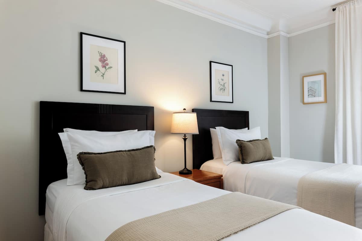 A hotel room with two beds, a nightstand with a lamp, and framed artwork on the walls.