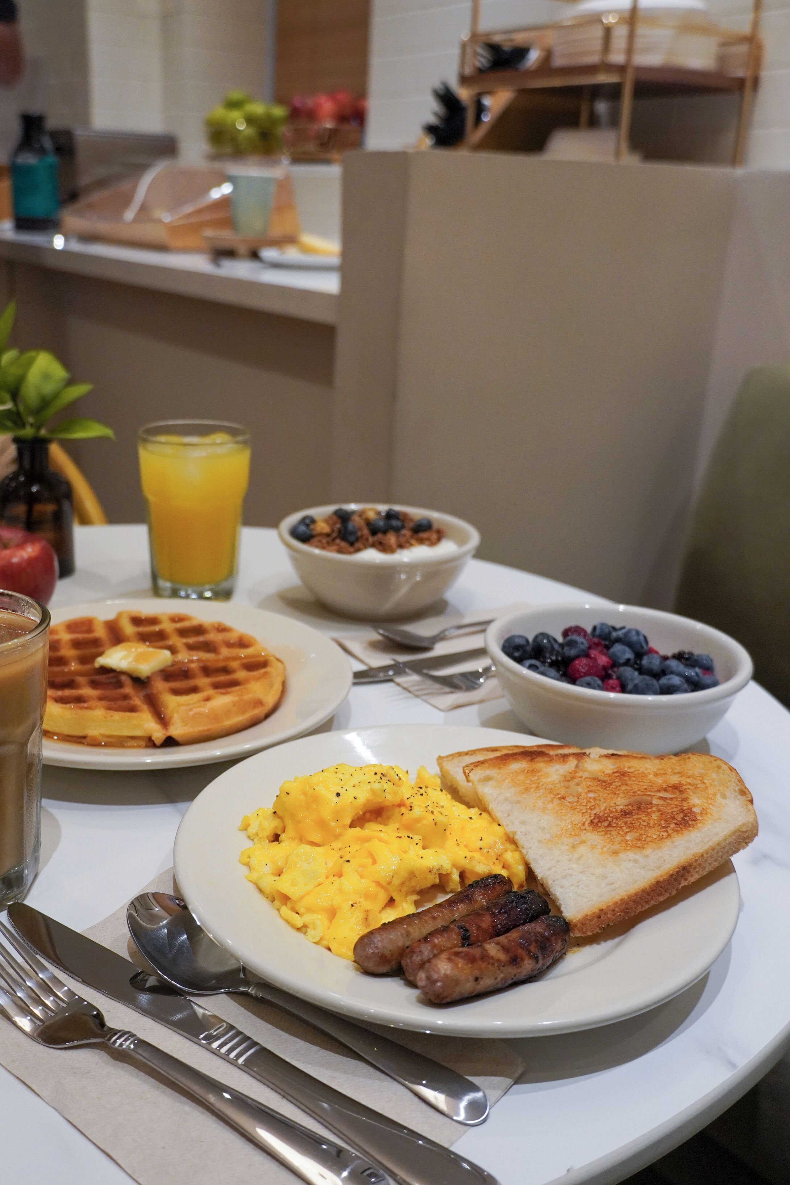 A breakfast setting with waffles, scrambled eggs, toast, sausages, and a bowl of blueberries.