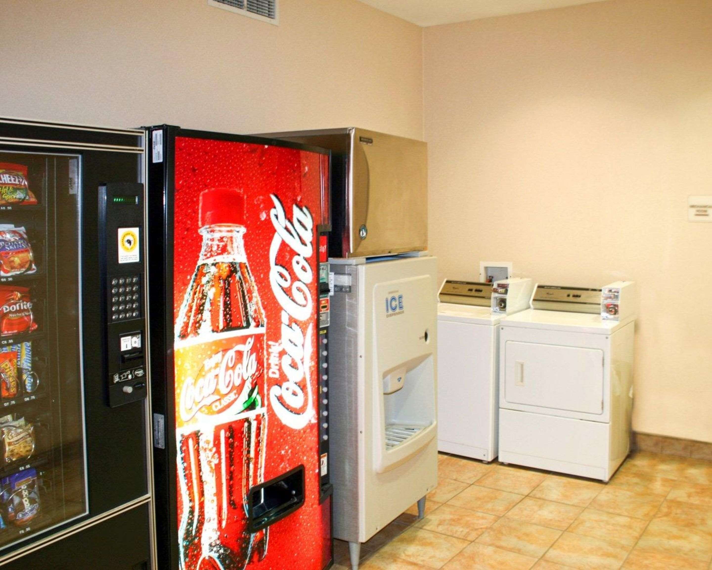 Máquina expendedora con logotipo de Coca-Cola, un refrigerador y un pequeño generador de hielo en una habitación con paredes color beige y piso de baldosas.