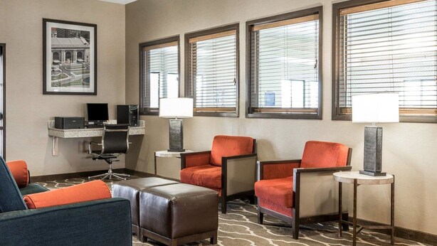 A hotel room with a desk, two chairs, a sofa, and a patterned carpet.