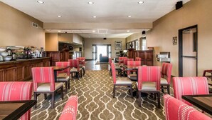 A hotel dining area with multiple tables and chairs, a kitchen area, and a view of the lobby.