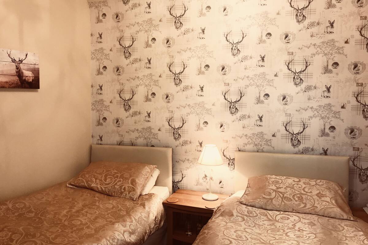 Ein Zimmer mit zwei Betten, einem Nachttisch und einer Wand mit einem Muster von Hirschen und Hasen.