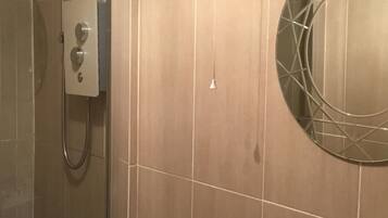 Een badkamer met een douche, een bedieningspaneel en een ronde spiegel aan de muur.