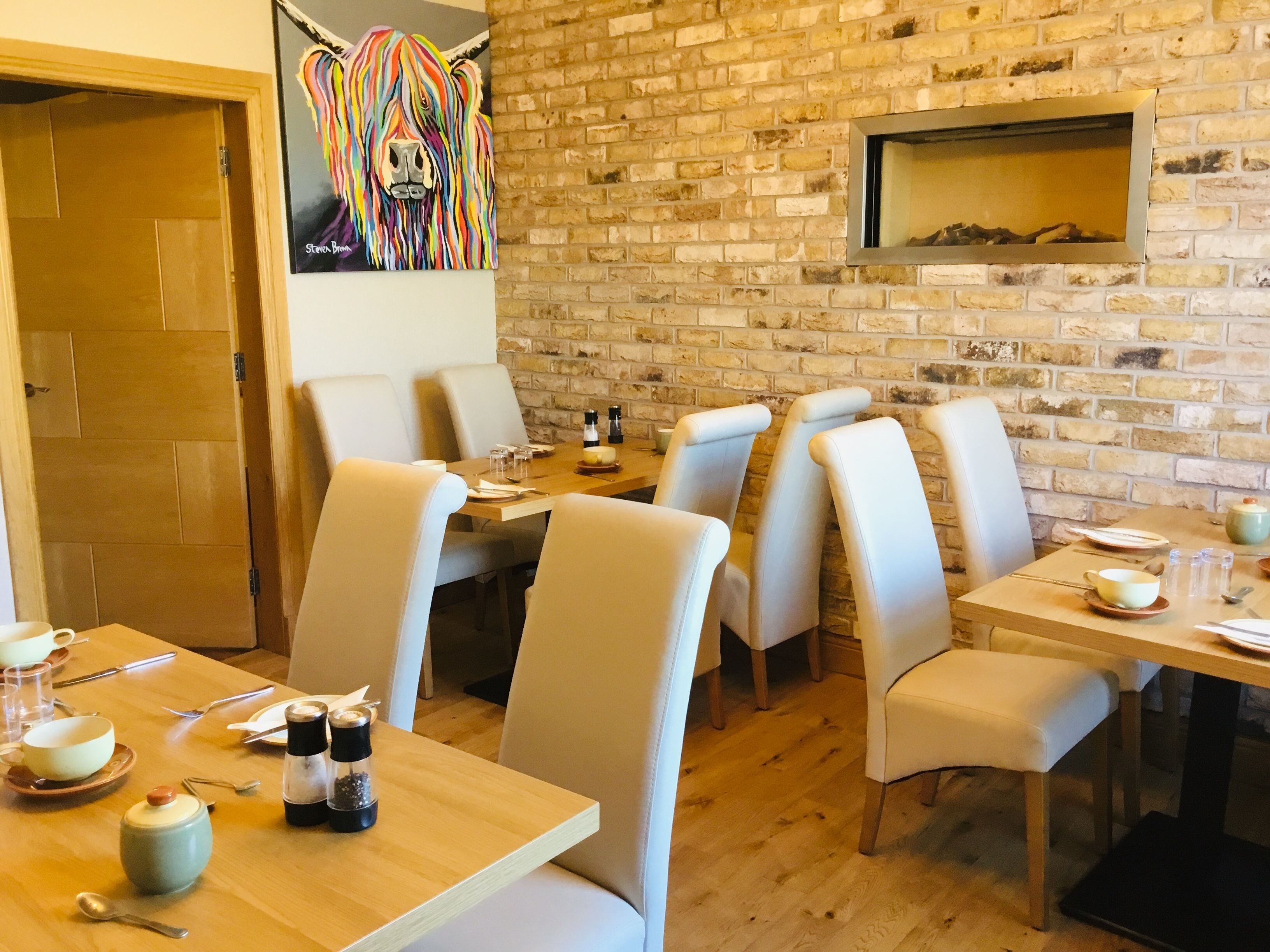 A restaurant with brick walls, wooden tables, and beige chairs.