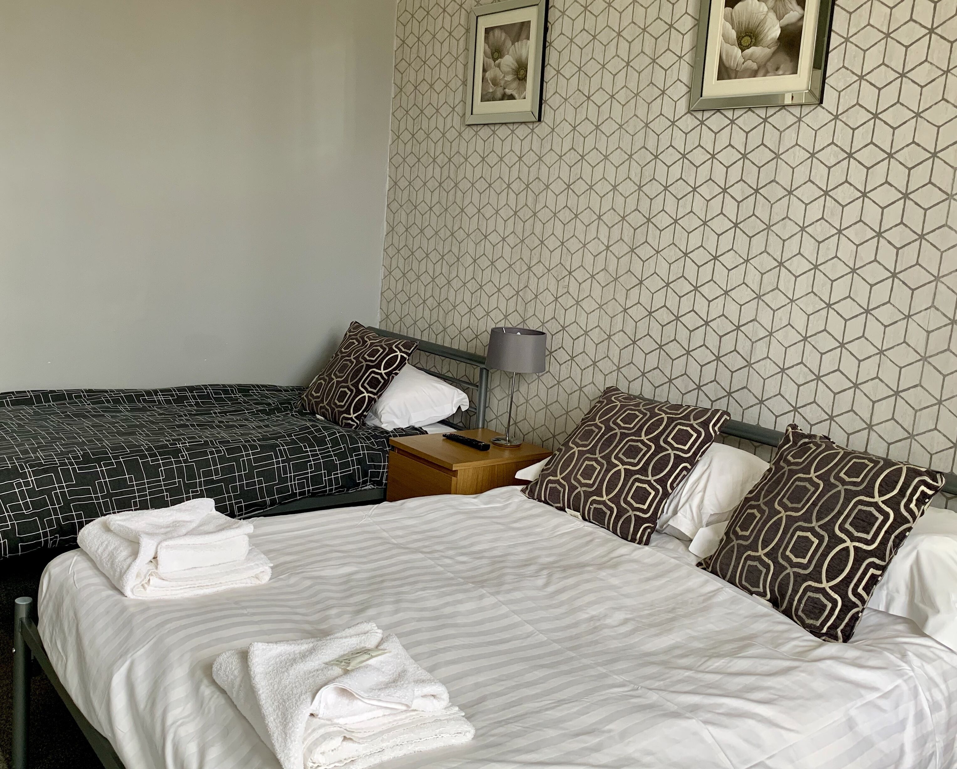 Une chambre d’hôtel avec deux lits, une table de chevet avec une lampe et un papier peint à motifs.
