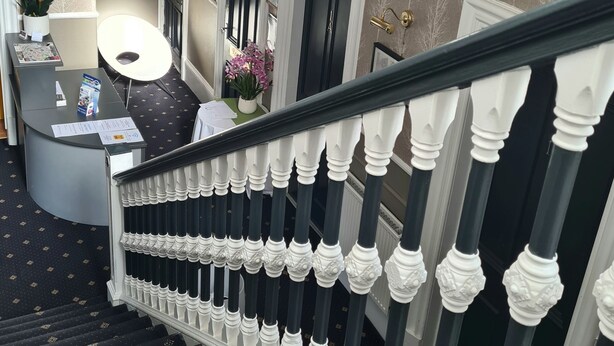 A staircase with ornate balusters, a reception desk with a vase of flowers, and a patterned carpet. - Northumberland Hotel (Edinburgh)