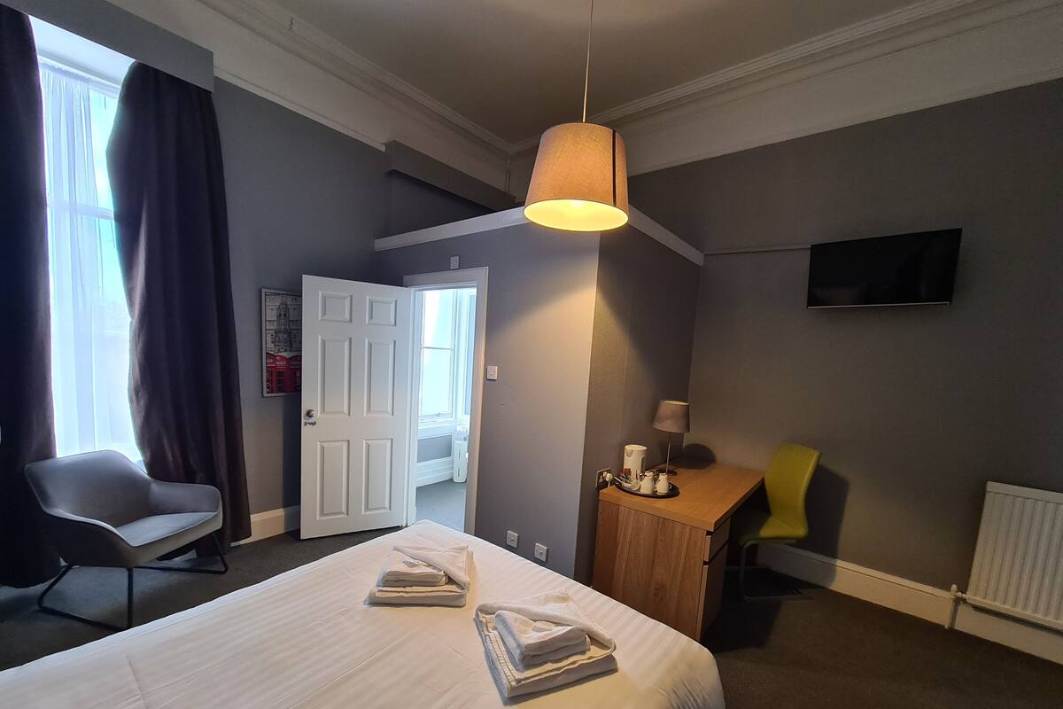 A hotel room with a bed, a desk, a chair, a television, and a door leading to another room.