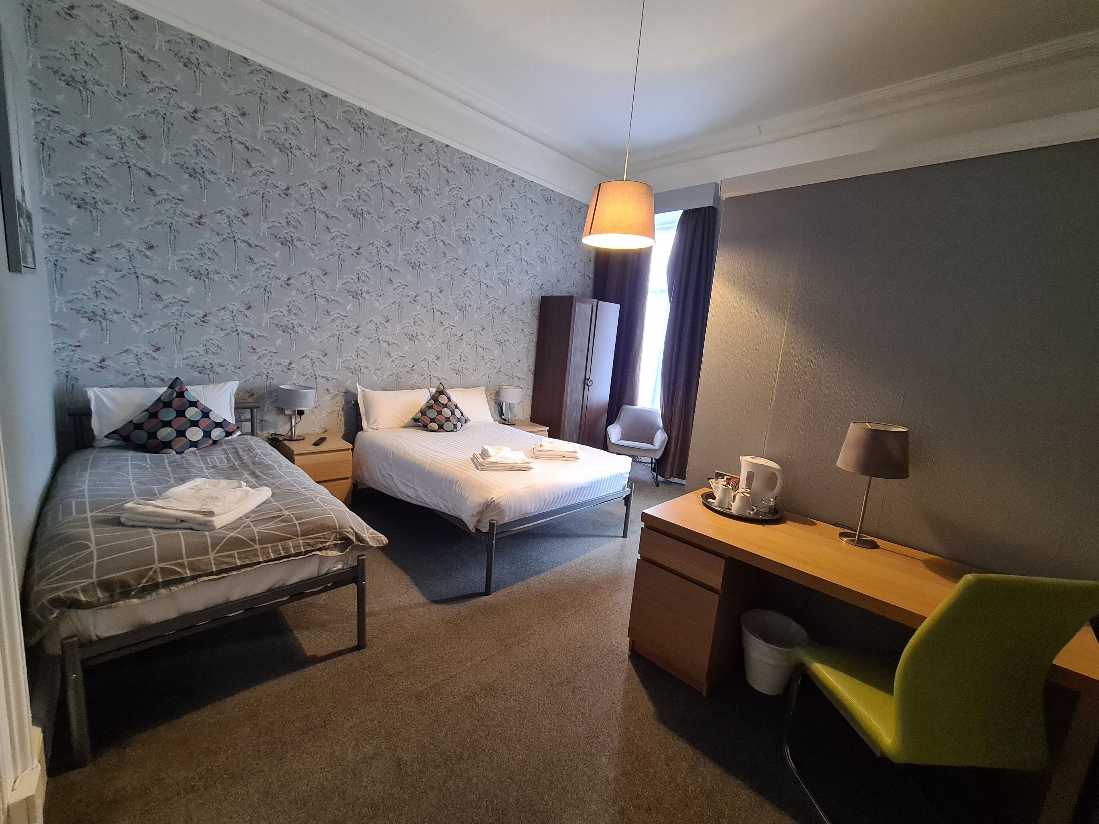 A hotel room with two beds, a desk, a chair, and a hanging lamp.