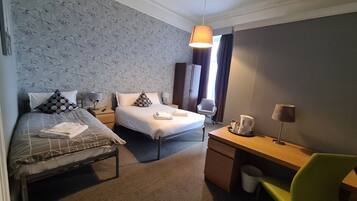 A hotel room with two beds, a desk, a chair, and a hanging lamp.