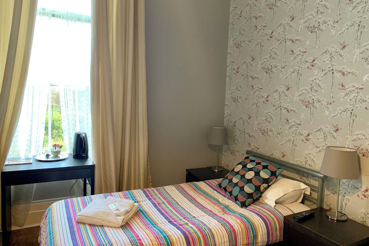 A hotel room with a bed, a nightstand, a lamp, and a window with curtains.