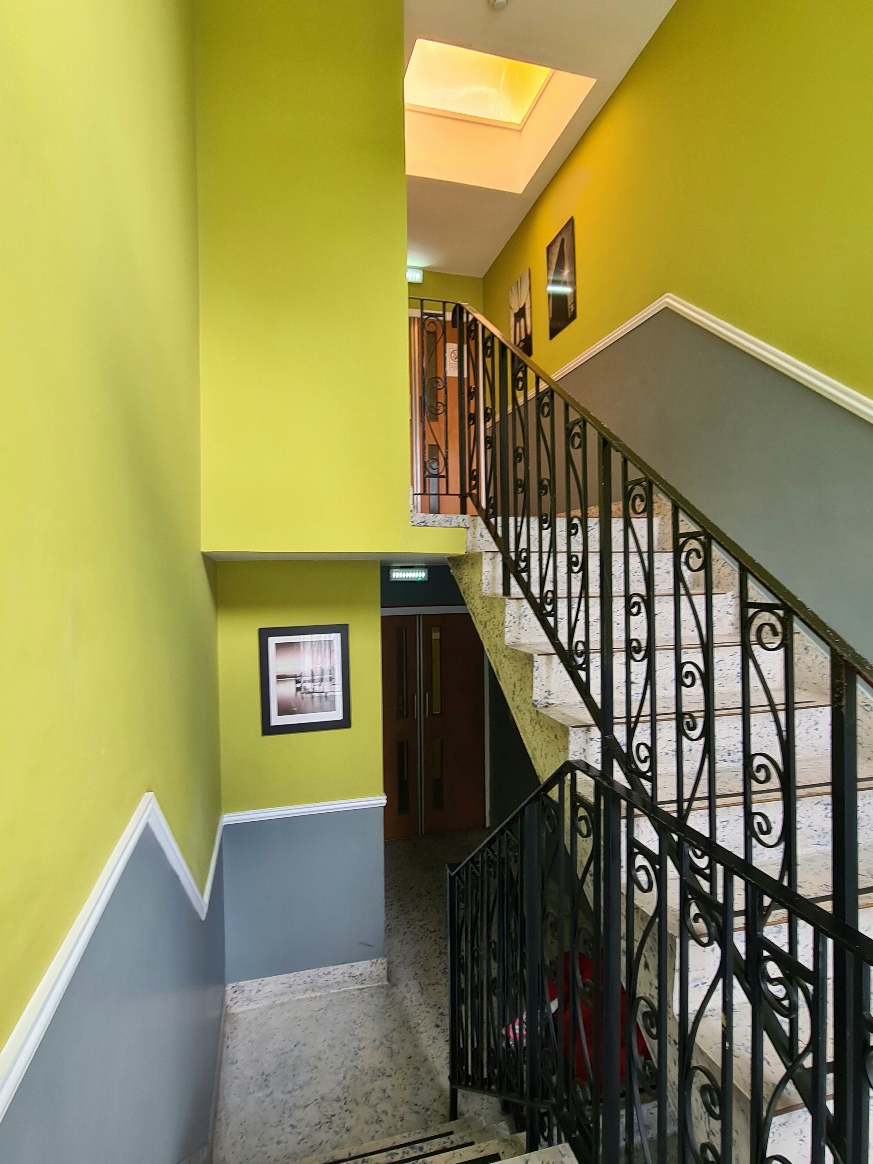 Un escalier avec des rampes en fer noir et un mur jaune.