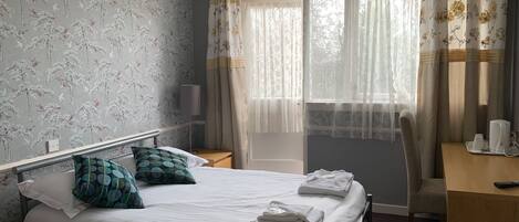 A hotel room with a bed, a desk, a chair, a lamp, and a window with curtains.