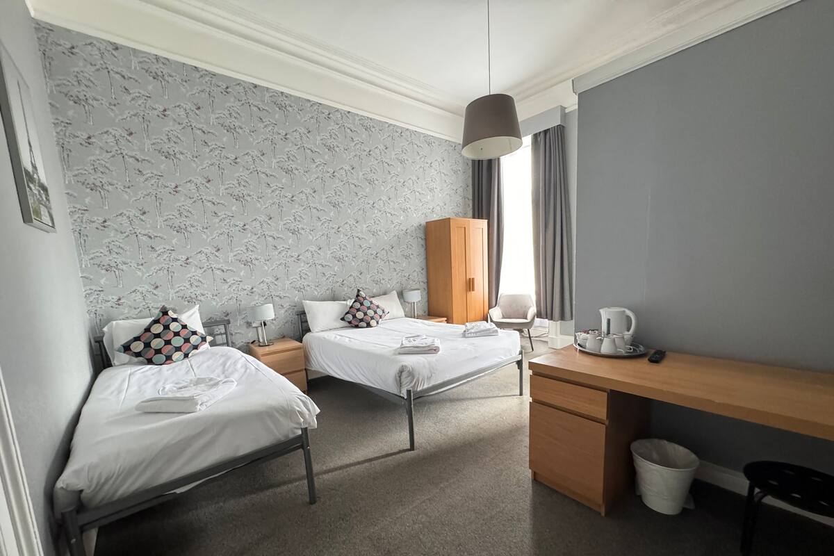 A hotel room with two beds, a desk, a wardrobe, and a coffee maker.