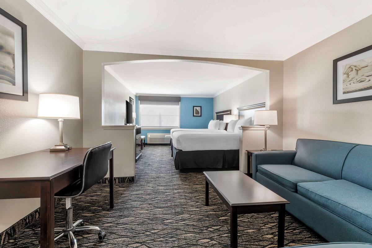 A hotel room with a bed, a desk, a chair, a sofa, and a lamp.