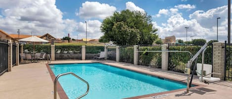 Una piscina rectangular con una escalera de metal, rodeada por un muro de ladrillo y una cerca de metal.