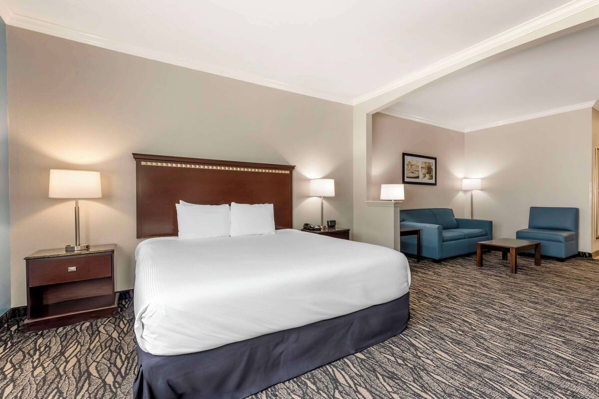 A hotel room with a large bed, two bedside tables with lamps, a blue sofa, and a small table.