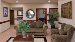 A living room with a sofa, armchair, and a coffee table. There is a potted plant and a mirror on the wall. - Americas Best Value Inn & Suites San Benito (San Benito)