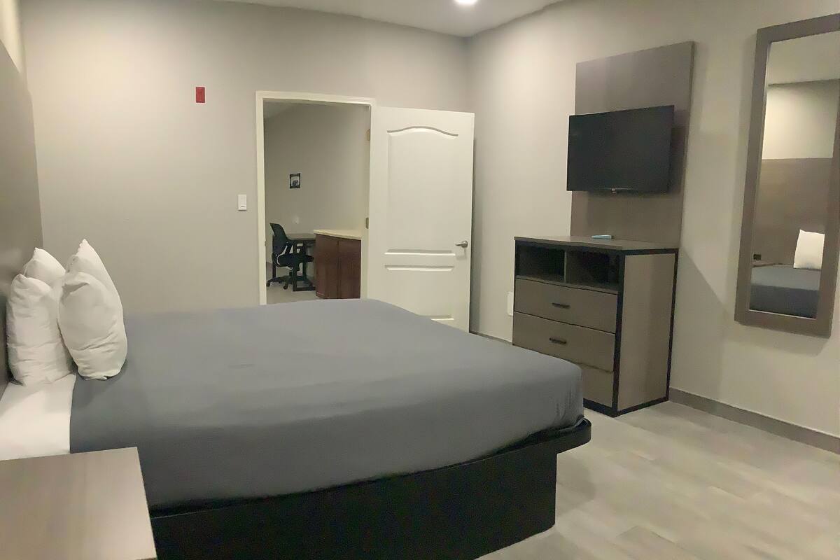 A bedroom with a bed, a dresser, a TV, and a mirror.