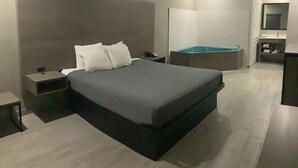 A modern hotel room with a large bed, bedside tables, a small desk, a built-in bench, and a bathroom with a mirror and sink. - Americas Best Value Inn & Suites San Benito (San Benito)