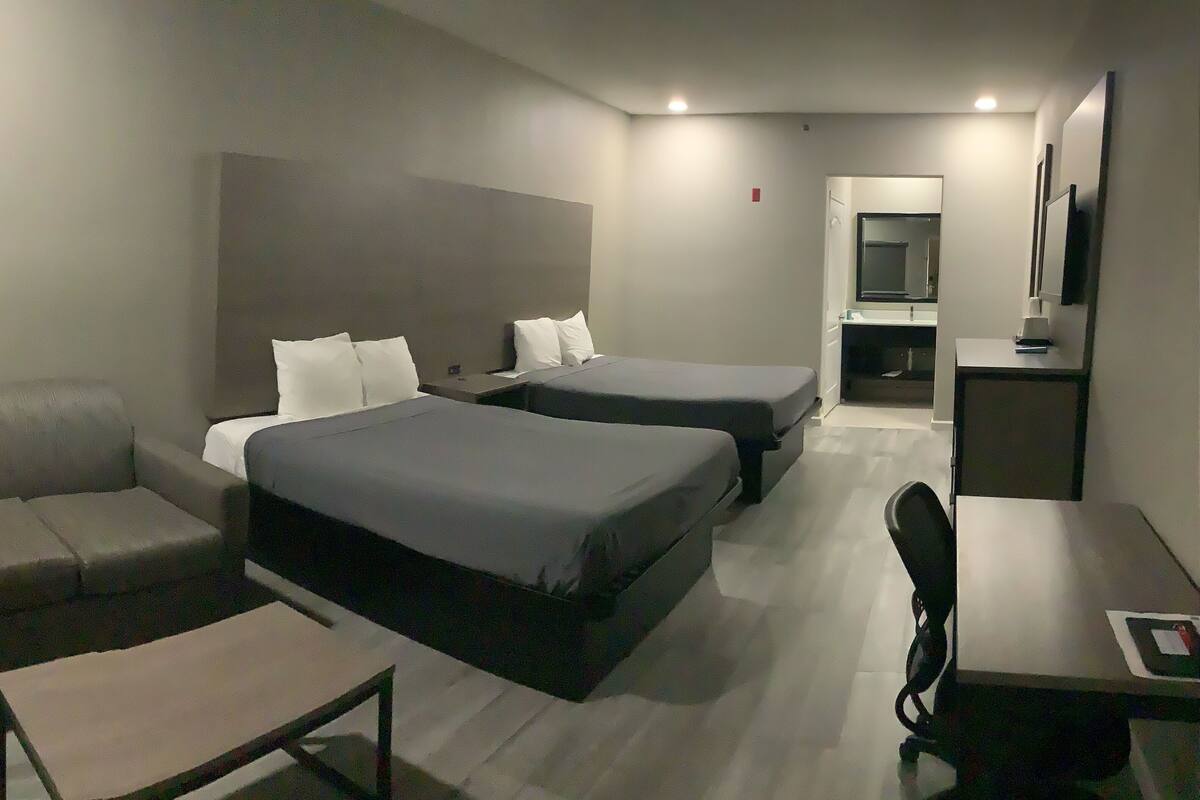 Una habitación de hotel con sofá, dos camas, un escritorio y un espejo.