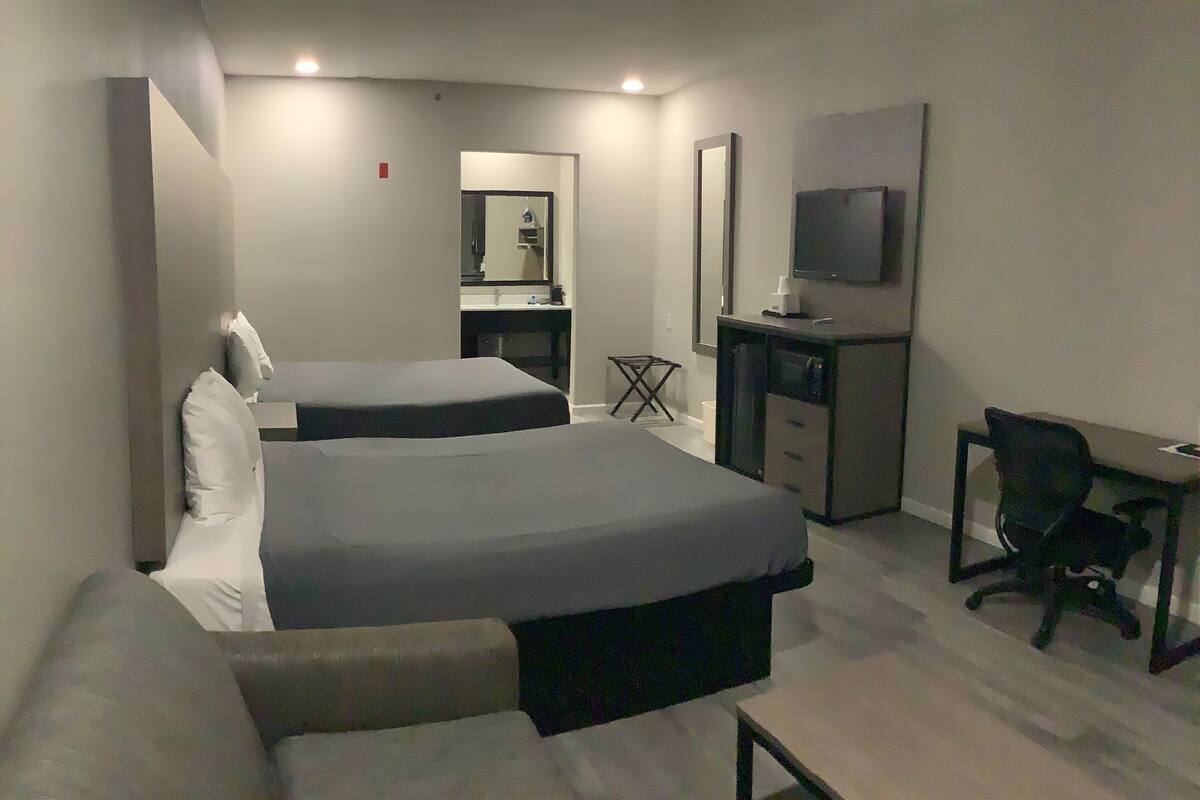A hotel room with two beds, a desk, a chair, a TV, and a small table.
