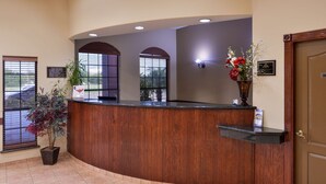 A reception area with a wooden reception desk, potted plants, and a door. - Americas Best Value Inn & Suites San Benito (San Benito)