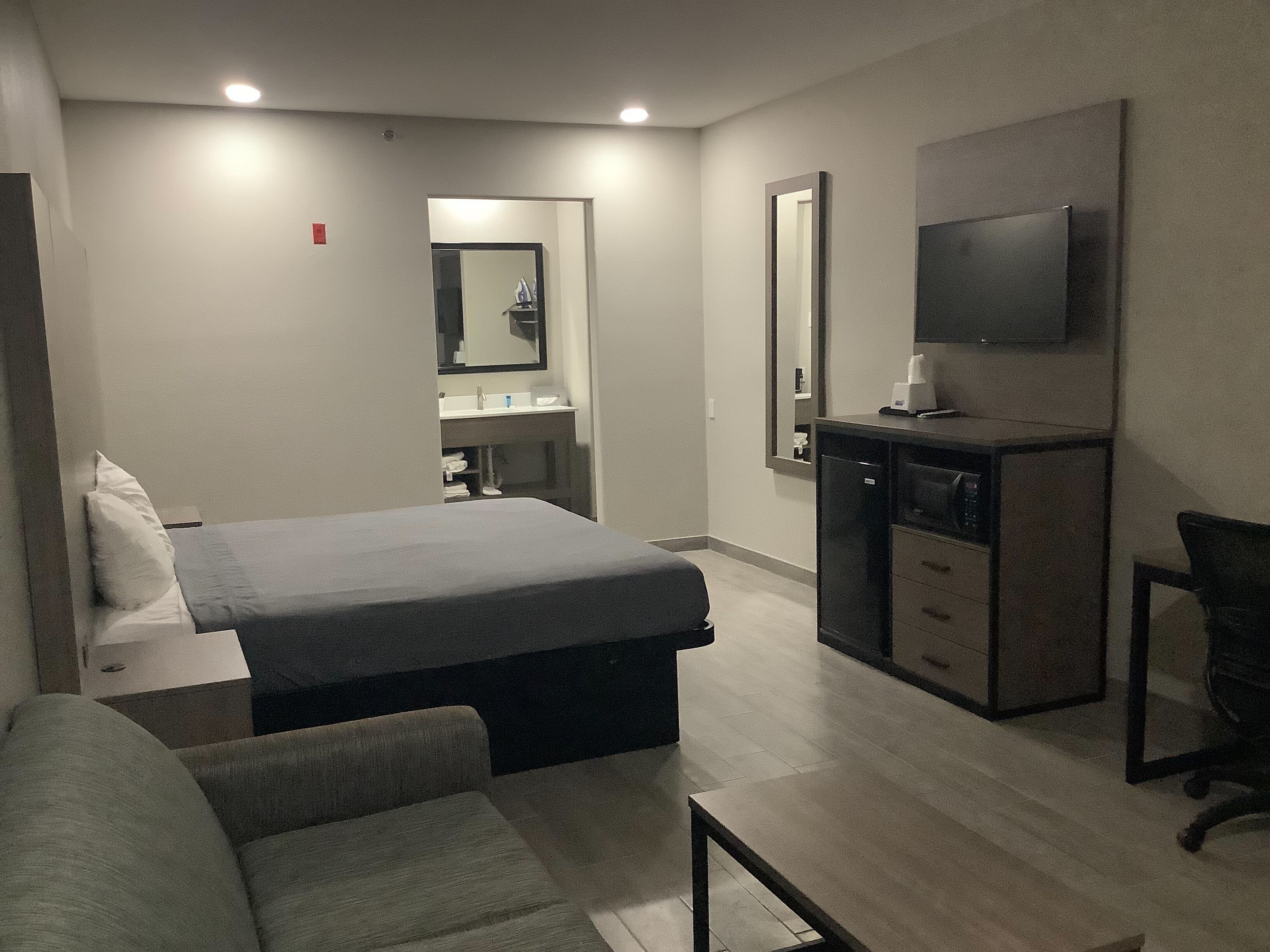 A hotel room with a bed, a desk, a chair, a TV, and a mirror.