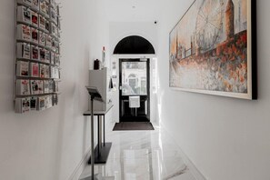 A hallway with a white wall, a magazine rack, a painting, and a door leading to another room. - Holiday City Ltd (London)