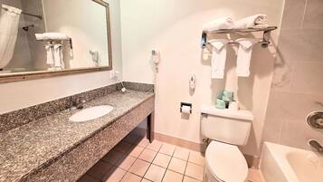 A bathroom with a granite countertop sink, a toilet, a shower, and a mirror.