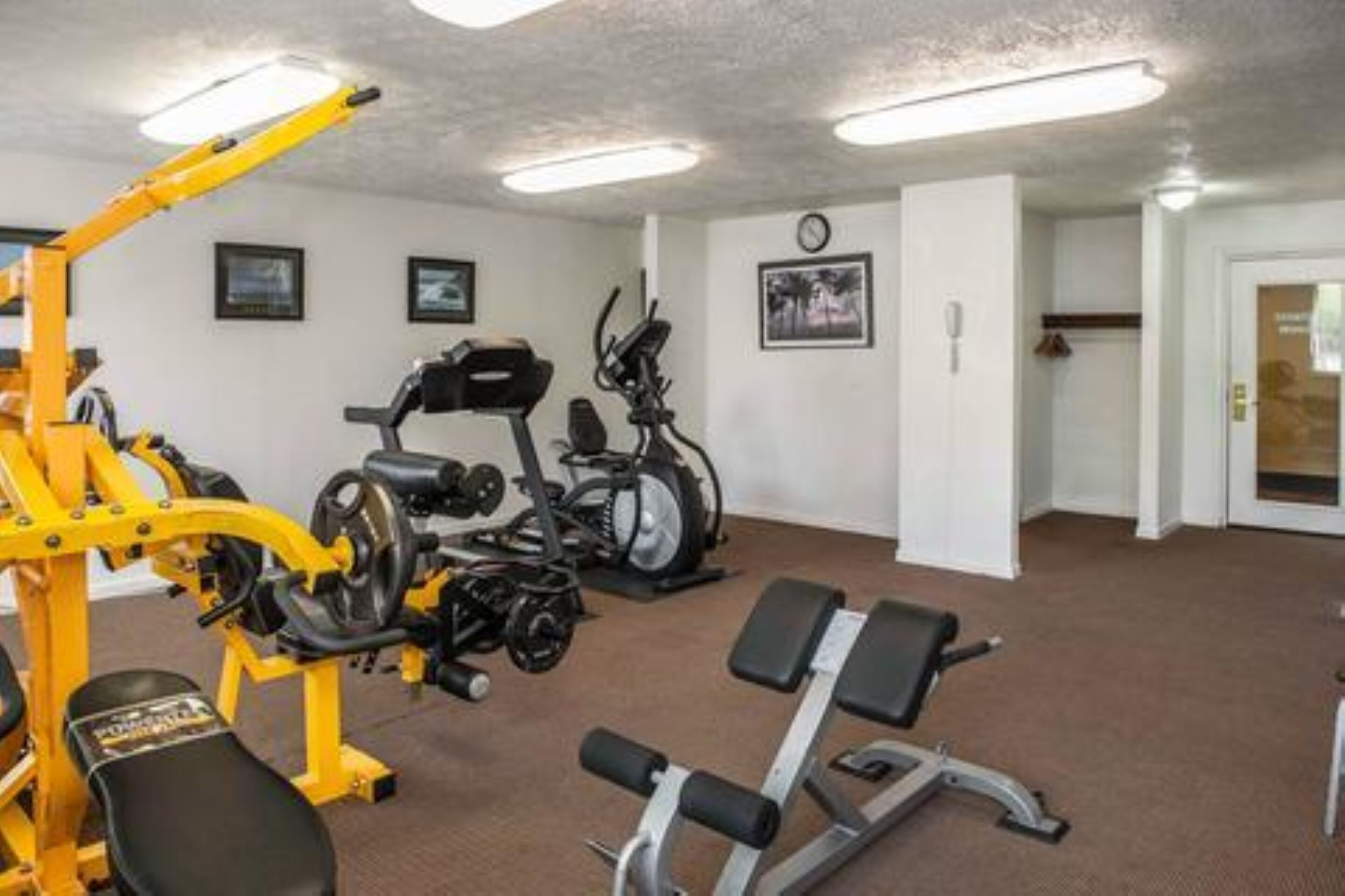 A gym with exercise equipment, a bench, and a clock on the wall.