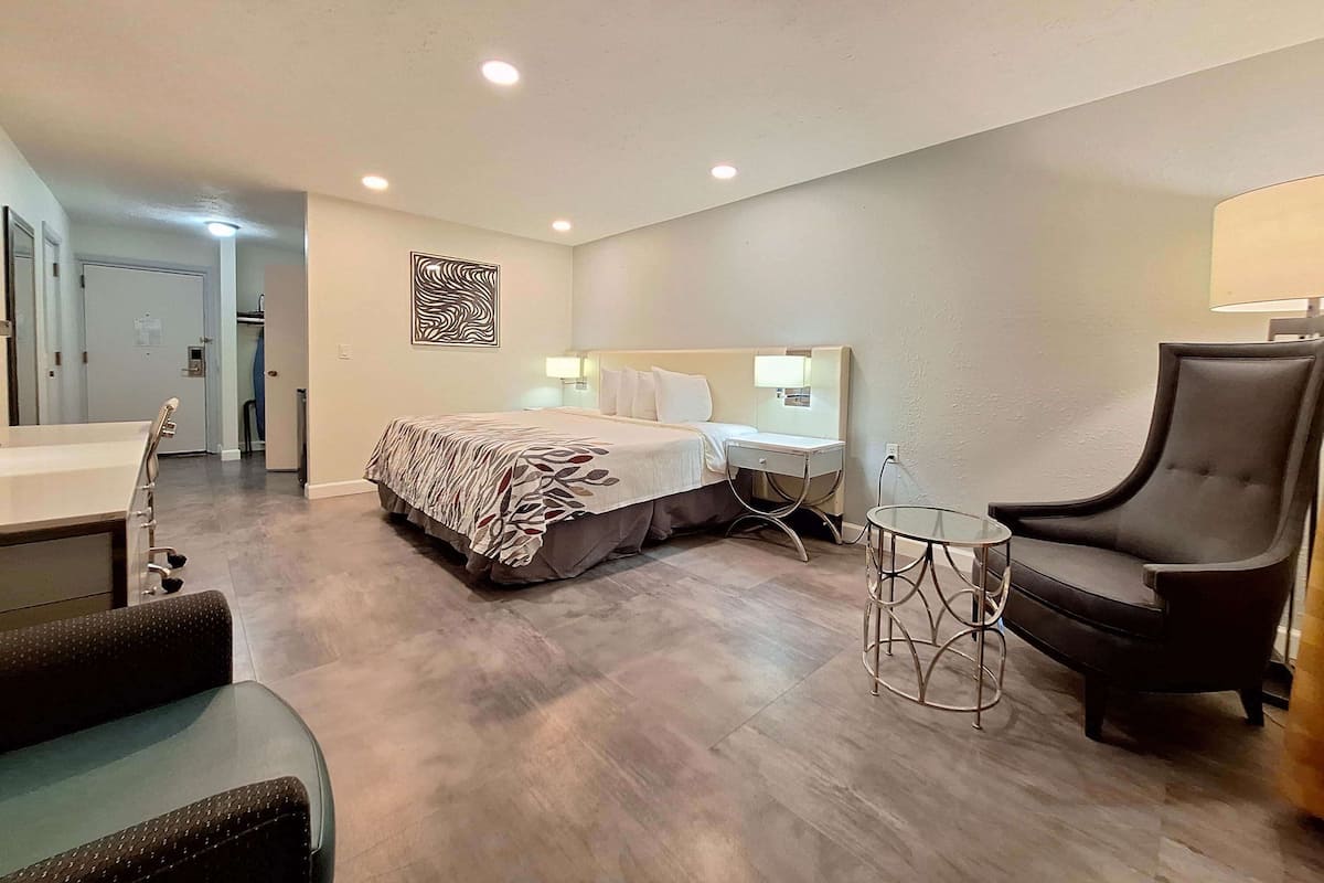 Une chambre d’hôtel avec un lit, une chaise, une petite table et une salle de bain équipée d’un lavabo et d’un miroir.