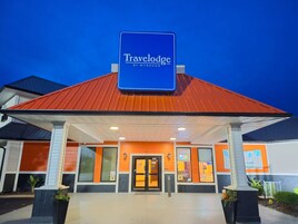 Entrada de un hotel Travelodge con techo rojo, fachada naranja y blanca, y un letrero azul.