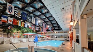 Una piscina interior con múltiples carriles, sillones reclinables y sombrillas. Banderas de varios países decoran el techo.