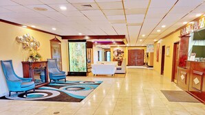 Un hall de hotel con una recepción, un área de descanso con sillas, una alfombra decorativa y una pantalla de televisión.