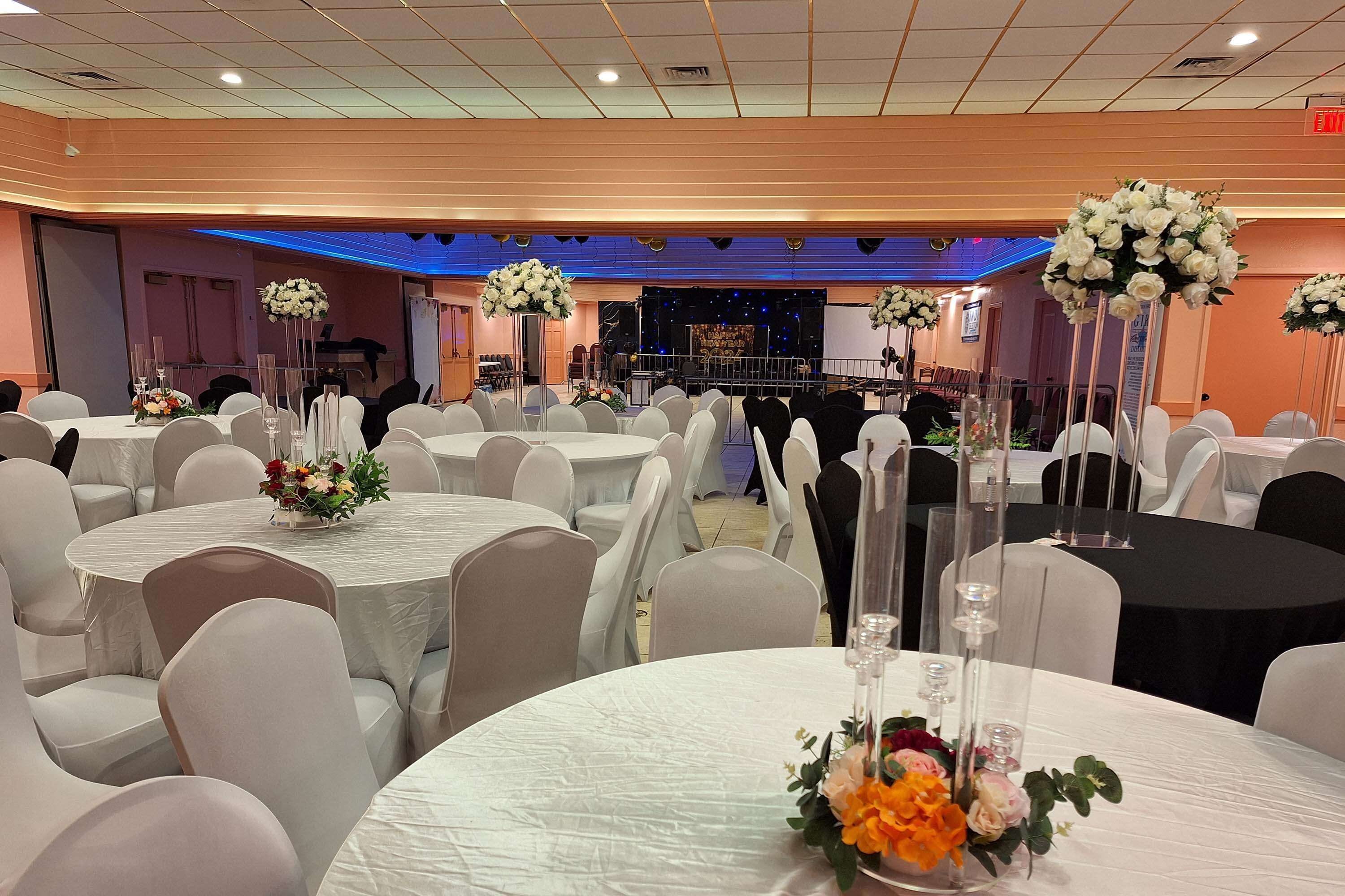 A banquet hall with round tables, white chairs, and floral centerpieces.