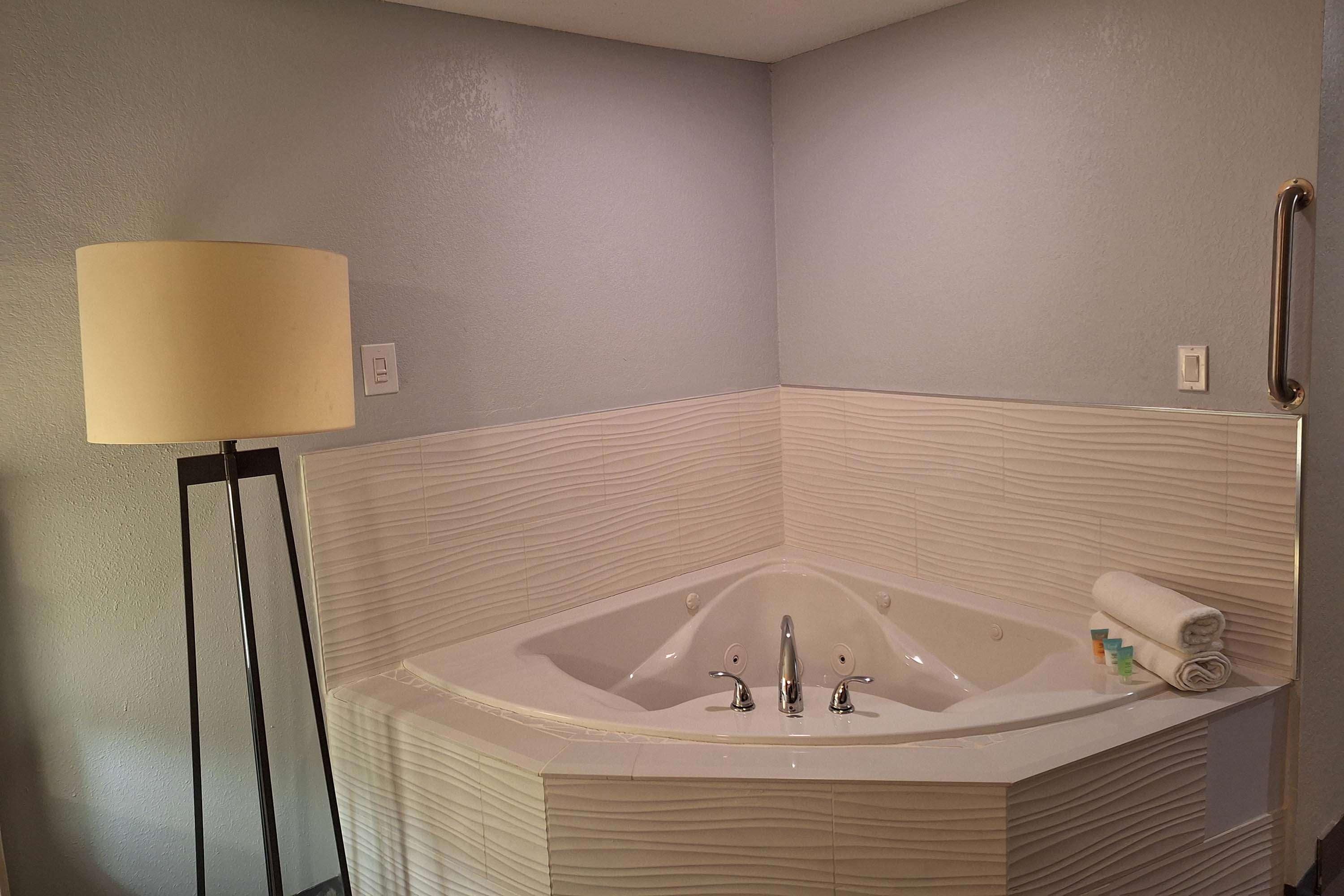 Un bagno angolare con una vasca da bagno freestanding, una lampada da terra e un asciugamano su un lato.